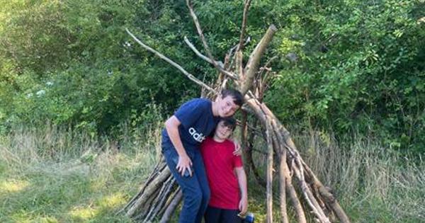 Two children stood in front of a den made of tree branches