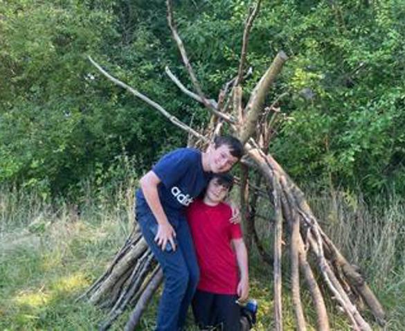 Two children stood in front of a den made of tree branches